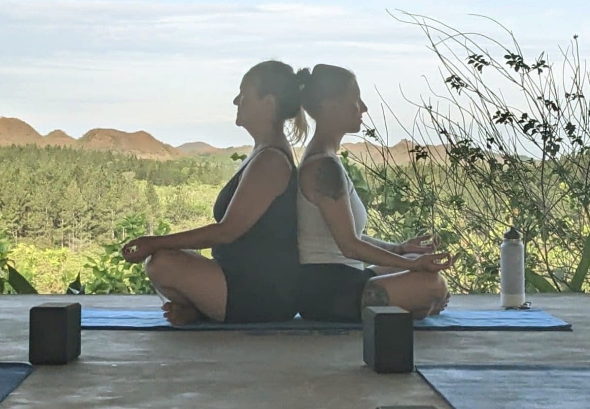 Two women sitting on a mat in the middle of their yoga practice.